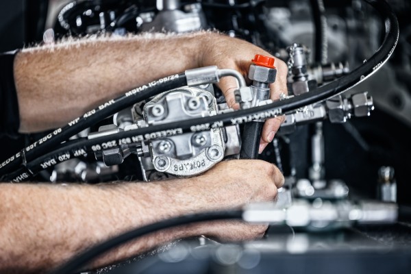 Businessfotografie zeigt die Hand eines Montagearbeiters bei der Montage der Hydraulikleitungen.